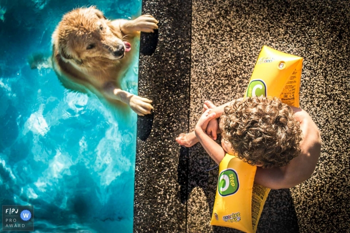 A boy sits by the edge of a pool watching his dog swim in this family picture by a Sao Paulo, Brazil photographer. 