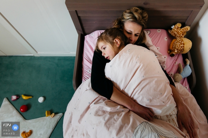Photo by: <a href="https://www.fpja.com/documentary-family-photography-contests/estelle-chhor/h%C3%A9rault/2066036">Estelle Chhor - France</a> A daughter lays in her bed with her mother in this photo recorded by a Herault award-winning, documentary-style family photographer.