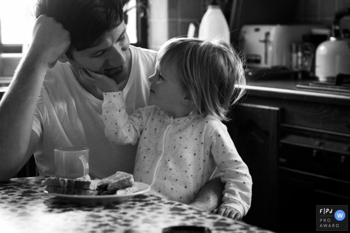 A daughter touches her father's face as they sit together eating breakfast in this Family Photojournalist Association contest awarded photo created by a Scotland family photographer. 