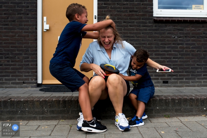Photo by: <a href="https://www.fpja.com/documentary-family-photography-contests/gonda-meurs/noord-holland/2066216">Gonda Meurs - Netherlands</a> Two little boys tackle their mother as she sits outside in this documentary-style family photo captured by a Netherlands photographer.