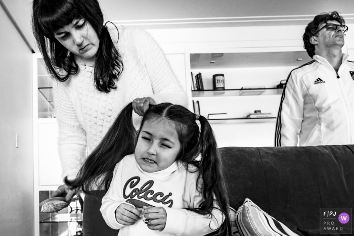 Photo by: <a href="https://www.fpja.com/documentary-family-photography-contests/renato-mello/rio-grande-do-sul/2066406">Renato Mello - Brazil</a> A girl winces as her mother puts her hair in pigtails in this FPJA award-winning image captured by a Rio Grande do Sul, Brazil family photographer.