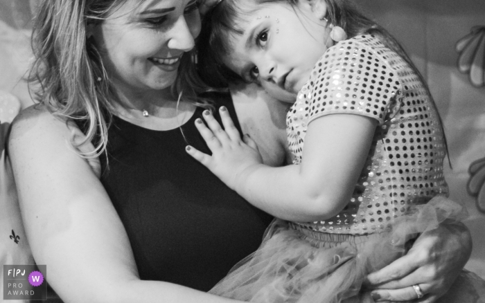 Une mère tient sa petite fille qui pose sa tête sur l'épaule de sa mère sur cette photo prise par un photographe de famille de style documentaire, lauréat d'un prix Arapongas.