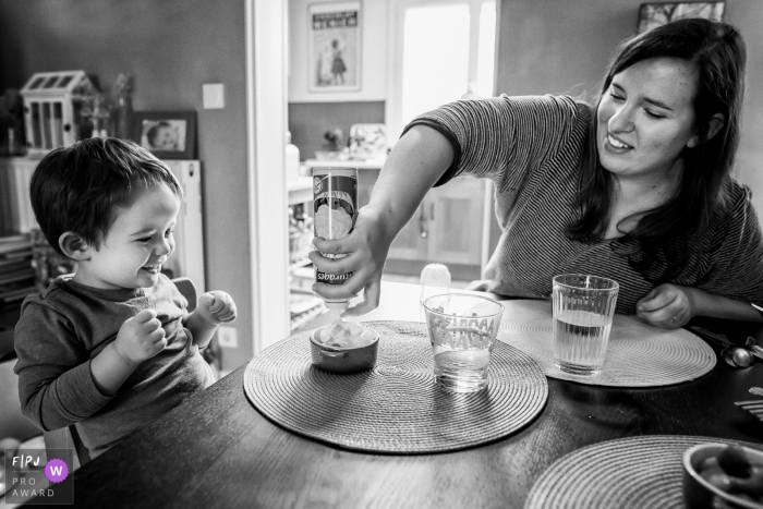 Photo by: <a href="https://www.fpja.com/documentary-family-photography-contests/maryline-krynicki/%C3%AEle-de-france/2066786">Maryline Krynicki - France</a> A little boy excitedly watches as his mother puts whipped cream on his dessert in this photograph created by a France family photojournalist.