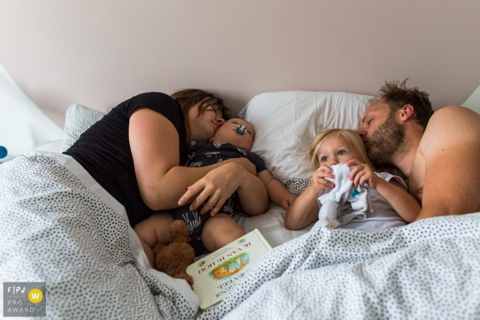 A mother and father cuddle with their children in bed in this Family Photojournalist Association awarded photo by a Modena documentary family photographer.