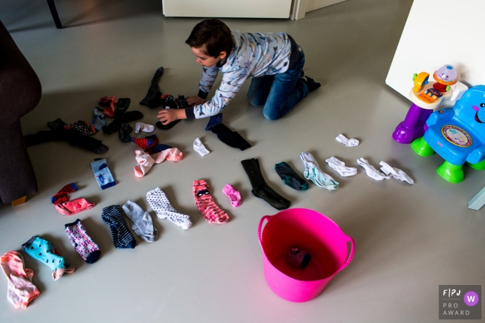 Photo by: <a href="https://www.fpja.com/documentary-family-photography-contests/lavinia-nitu/modena/2067321">Lavinia Nitu - Italy</a> A boy works on folding socks in this FPJA award-winning image captured by a Modena family photographer.