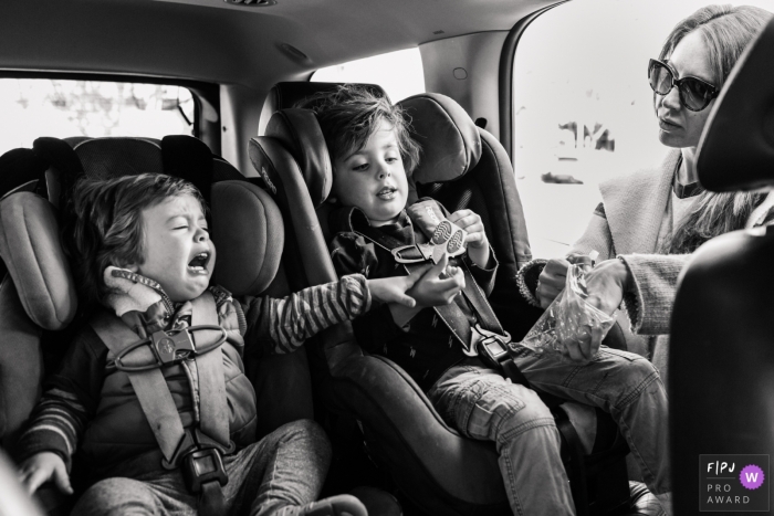 Photo by: <a href="https://www.fpja.com/documentary-family-photography-contests/melissa-mcclure/los-angeles/2068101">Melissa McClure - United States</a> A mother gets a snack for her sons sitting in their car seats in this Family Photojournalist Association awarded photo by a Los Angeles, CA documentary family photographer.