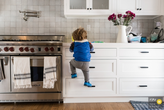 Un petit garçon grimpe aux tiroirs de la cuisine pour se rendre au comptoir dans cette image primée du FPJA, capturée par un photographe de famille à Los Angeles, en Californie.