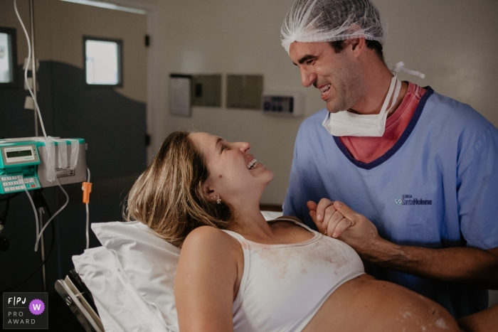 Un mari tient la main de sa femme à l'hôpital alors qu'elle accouche sur cette photo prise par un photographe de naissance de Florianopolis.