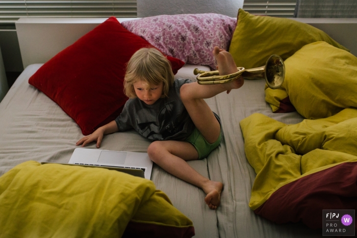 A boy plays with his trumpet on his foot in this Family Photojournalist Association contest awarded photo created by a Netherlands family photographer. 