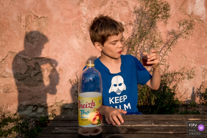 A boy looks uncertainly at a drink in his hand in this Family Photojournalist Association awarded photo by a Nantes documentary family photographer.