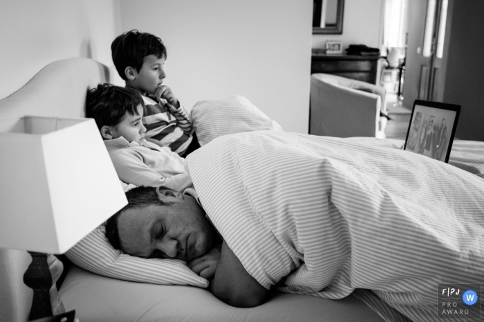 Two boys sit in bed while their father sleeps next to them in this award-winning photo by a Nantes family photographer.