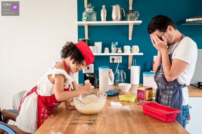 Photo by: <a href="https://www.fpja.com/documentary-family-photography-contests/sybil-rondeau/nantes/2068556">Sybil Rondeau - France</a> A father covers his eyes as his daughter adds an ingredient to their cookie batter in this picture captured by a Nantes family photojournalist.