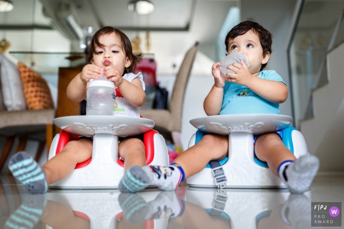 Photo by: <a href="https://www.fpja.com/documentary-family-photography-contests/priscilla-mondo/rio-de-janeiro/2068841">Priscilla Mondo - Brazil</a> A boy and girl eat and drink in their chairs on the floor in this family picture by a Sao Paulo, Brazil photographer.