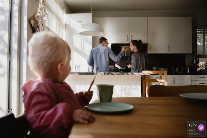 Photo by: <a href="https://www.fpja.com/documentary-family-photography-contests/charlene-van-der-gracht/amsterdam/2068941">Charlene van der Gracht - Netherlands</a> A husband has his wife taste what he is cooking as their baby sits at the kitchen table watching in this FPJA award-winning image captured by an Amsterdam family photographer.