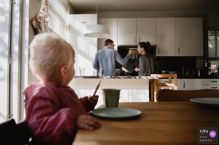 Un mari demande à sa femme de goûter à ce qu’il fait cuire pendant que leur bébé est assis à la table de la cuisine et regarde cette image primée du FPJA, capturée par un photographe de la famille d’Amsterdam.