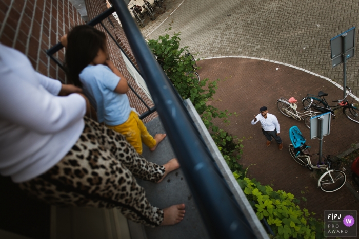 Photo by: <a href="https://www.fpja.com/documentary-family-photography-contests/charlene-van-der-gracht/amsterdam/2068981">Charlene van der Gracht - Netherlands</a> A father waves up to his wife and daughter on a balcony in this award-winning photo by an Amsterdam family photographer.