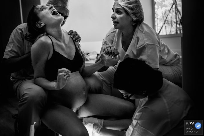 Two nurses help a woman during her home birth in this black and white birth image captured by a Rio de Janeiro, Brazil photographer.