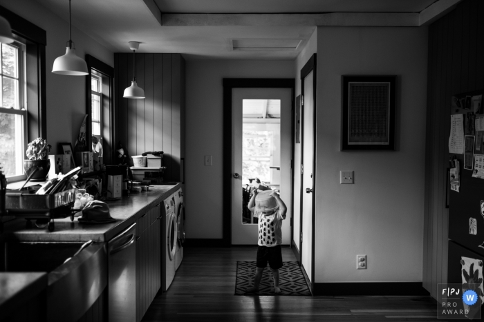 A little boy plays in the kitchen with a plastic container on his head in this Family Photojournalist Association contest awarded photo created by a Boston, MA family photographer. 