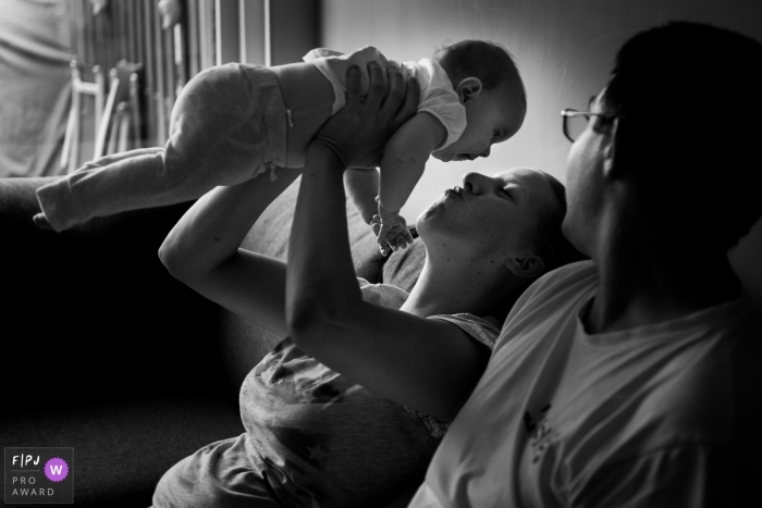 A mother holds her baby in the air as her husband watches in this family picture by an Amsterdam photographer. 