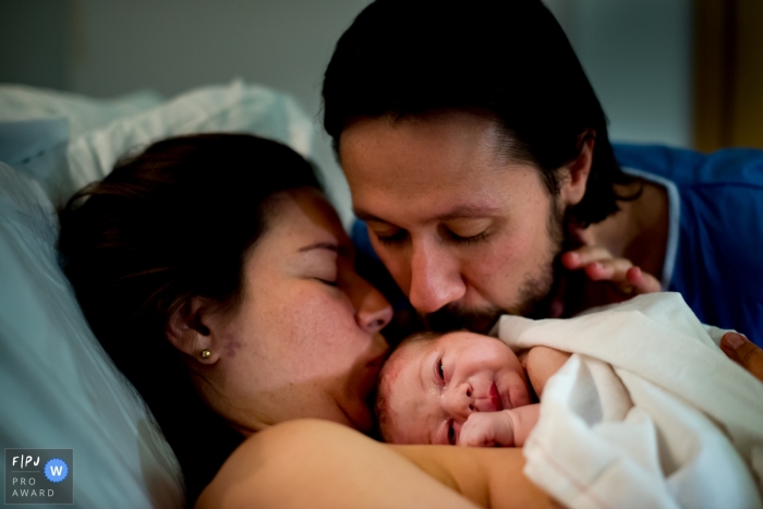 Une mère et un père embrassent leur nouveau-né à l'hôpital dans cette photographie de naissance prise par un photographe documentaire de Londres, en Angleterre.