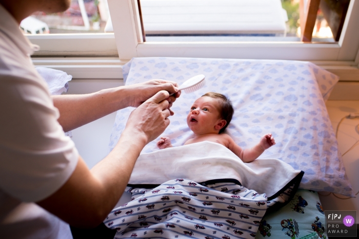 A baby is curious about a brush in this Family Photojournalist Association awarded photo by a London, England documentary family photographer.