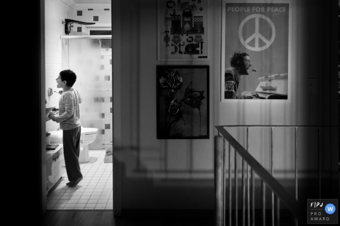 A little boy stands on tiptoe as he brushes his teeth in the bathroom in this award-winning photo by a London, England family photographer.