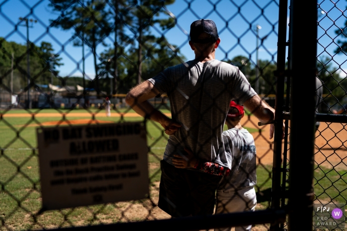 A son puts his arm around his father on the sidelines during a baseball game in this photo by an Atlanta, GA award-winning family photographer. 