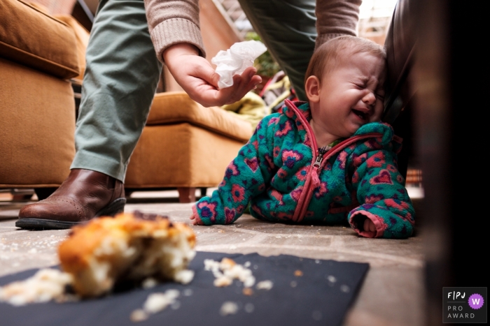 A father comforts his crying daughter who lays next to a cupcake that has fallen on the floor in this photograph created by an Atlanta, GA family photojournalist. 