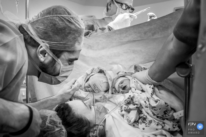 A mother and father hold their newborn twins in the hospital for the first time in this black and white photo by an award-winning Rio de Janeiro, Brazil birth photographer.