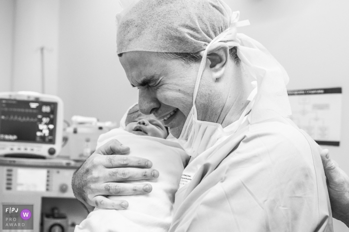 A father gets emotional as he holds his newborn infant in the hospital for the first time in this black and white photo by a Rio de Janeiro, Brazil documentary birth photographer.