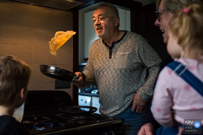 Un grand-père montre ses talents de cuisinier en retournant une crêpe dans cette image familiale de style documentaire enregistrée par un photographe néerlandais.