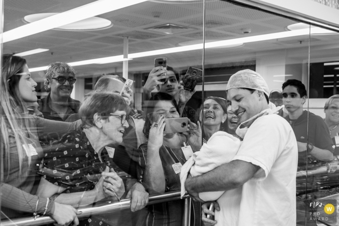 Une infirmière tient un bébé devant la fenêtre de l'hôpital pour que sa famille puisse la voir tandis qu'ils se rassemblent et prennent des photos sur cette photo de famille prise par un photographe de Rio de Janeiro, Brésil.