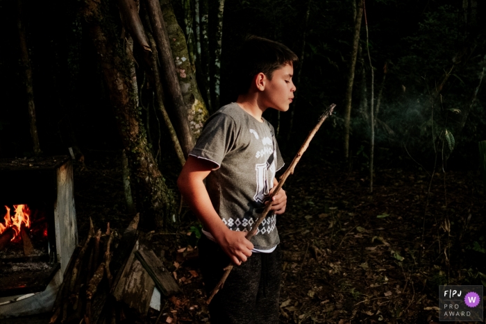 A boy blows out a flame on the end of a stick during a camping trip at night in this photograph created by a Florianopolis family photojournalist. 