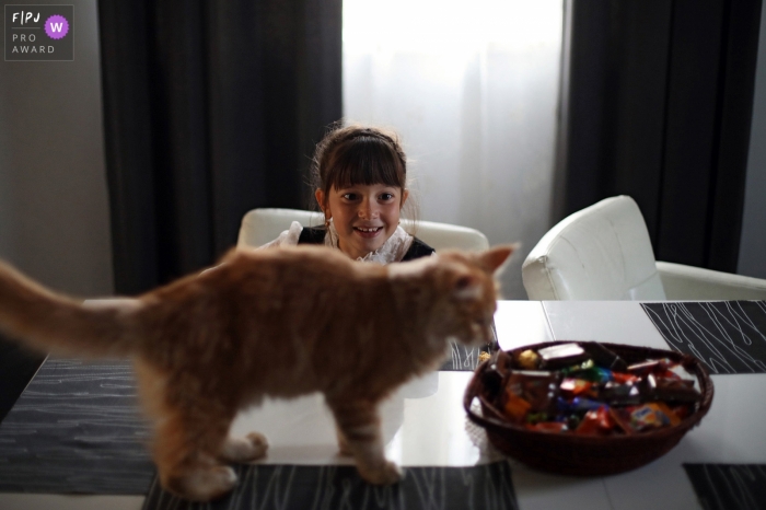 Photo by: <a href="https://www.fpja.com/documentary-family-photography-contests/elena-petrova/saint-petersburg/2071171">Elena Petrova - Russia</a> A little girl watches a kitten sniff a bowl of candy in this award-winning photo by a Saint Petersburg, Russia family photographer.