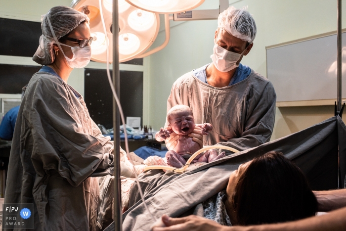 A doctor lets a mother see her baby for the first time after her C-section in this photo taken in the hospital by a Minas Gerais birth photographer.