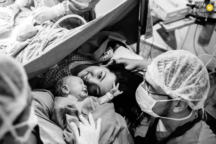 Photo by: <a href="https://www.fpja.com/documentary-family-photography-contests/val-goncalves/belo-horizonte/2071371">Val Goncalves - Brazil</a> A mother meets her infant for the first time in the hospital as the doctor closes her C-section in this photo by an award-winning Minas Gerais birth photographer.