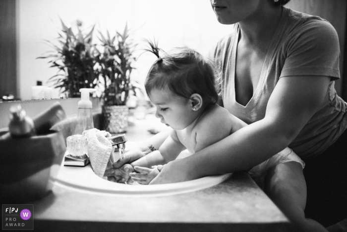 Une mère aide sa fille à se laver les mains dans cette image de famille de style documentaire enregistrée par un photographe de Seattle, WA.