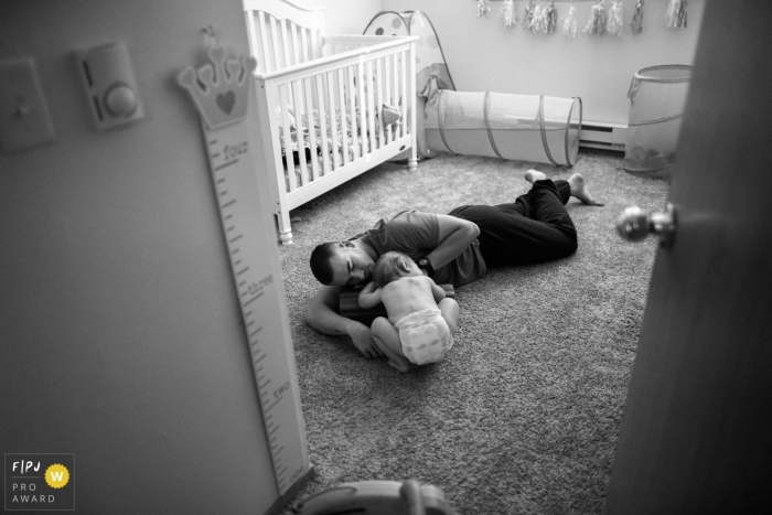 Photo by: <a href="https://www.fpja.com/documentary-family-photography-contests/ron-storer/seattle/2071721">Ron Storer - United States</a> A father lays on the floor with his baby in this Family Photojournalist Association contest awarded photo created by a Seattle, WA family photographer.
