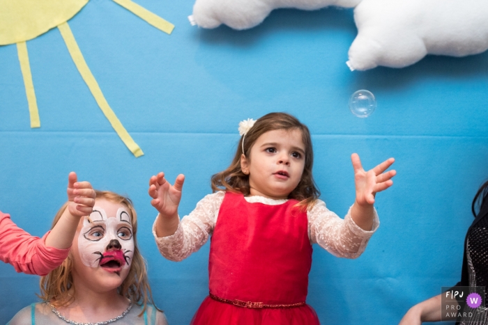 Une jeune fille essaie de faire éclater une bulle, tandis qu'une fille au visage peint représente sur cette photo un photojournaliste de la famille de Lisbonne, au Portugal.