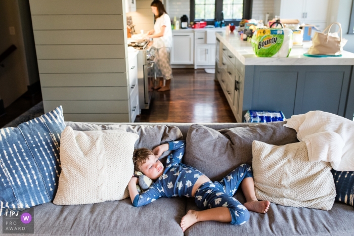 A boy lays sprawled on the couch as his mother cooks in the kitchen in this photo by a Missoula, MT family photojournalist.