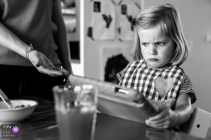 Photo by: <a href="https://www.fpja.com/documentary-family-photography-contests/sandra-van-der-meulen/noord-holland/2074116">Sandra van der Meulen - Netherlands</a> A little girl makes a face as her mother asks her to hand over the tablet she's playing on in this black and white photo by a Netherlands family photojournalist.