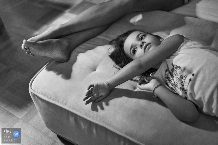 A girl lays on an an ottoman next to her mother's legs in this black and white photo by a Rome family photographer 