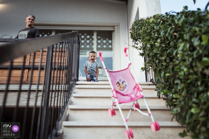 Photo by: <a href="https://www.fpja.com/documentary-family-photography-contests/fulvia-bernacca/rome/2074636">Fulvia Bernacca - Italy</a> A little boy watches the toy stroller he pushed down the steps in this photo by a Lazio family photojournalist.