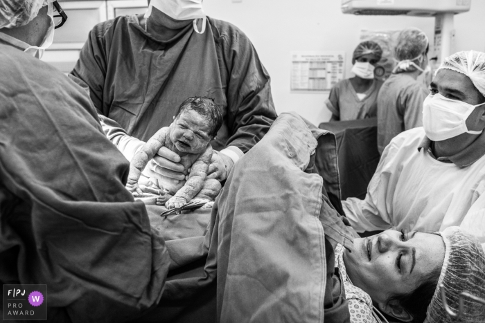 A doctor and nurse work on cleaning up a newborn immediately after birth in the hospital in this black and white photo by a Sao Paulo birth photographer.