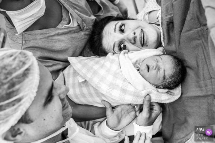 A doctor and nurse show a mother her newborn infant in the hospital for the first time in this black and white photo by a Sao Paulo birth photographer.