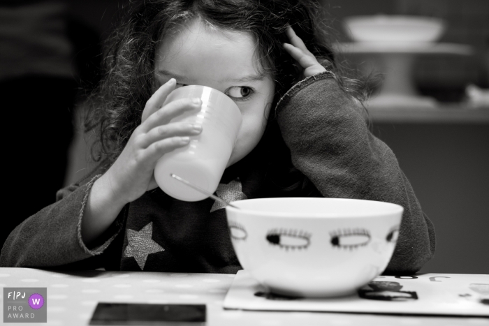 Une fille sirote une tasse en prenant son petit-déjeuner sur cette photo en noir et blanc réalisée par un photojournaliste de famille du Gloucestershire, en Angleterre.