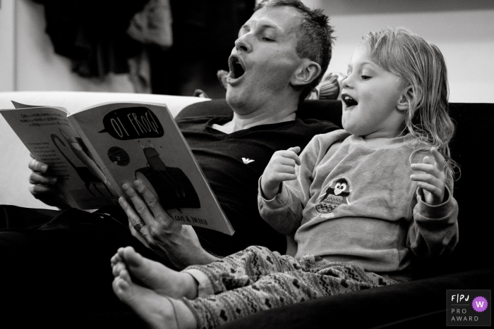 Un père et une fille ont lu avec enthousiasme un livre sur un canapé sur cette photo en noir et blanc réalisée par un photojournaliste de famille du Gloucestershire, en Angleterre.