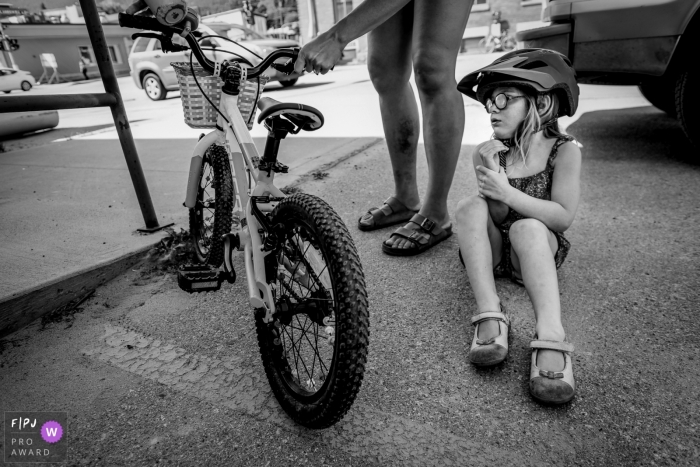 A little girl sits on the ground after falling off her bike in this black and white photo by a British Columbia, Canada family photojournalist. 