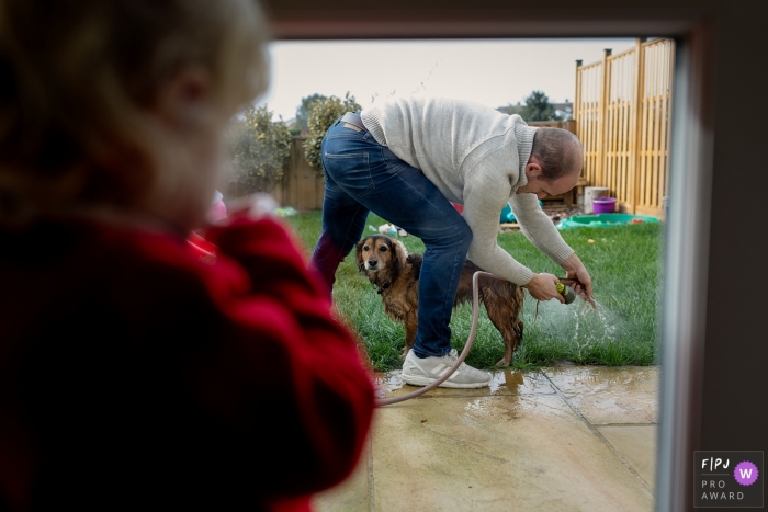 Photo by: <a href="https://www.fpja.com/documentary-family-photography-contests/catherine-hill/kent/2077406">Catherine Hill - United Kingdom</a> A little girl watches her father hose down their dog outside in this photo by a Kent, England family photojournalist.