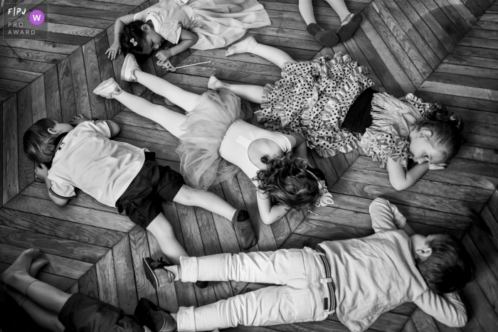 Several children lay on their stomachs on a wood floor in this black and white photo by a France family photojournalist. 